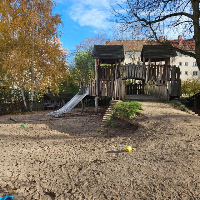 Außenspielplatz mit Holzkonstruktion, Rutsche und Sand.