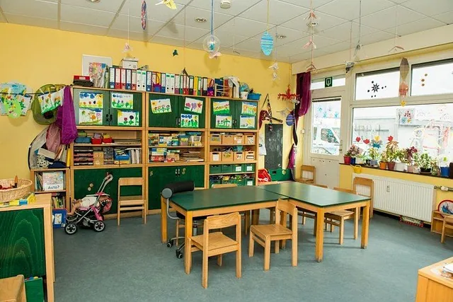 Heller, organisierter Kinderklassenraum mit Tischen und Regalen.
