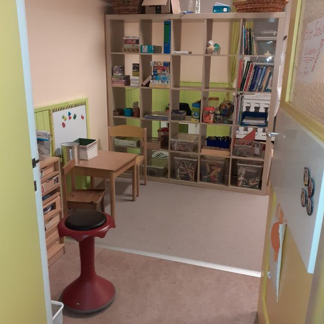 Kinderspielzimmer mit Regalen, Tisch und Sitzgelegenheiten.