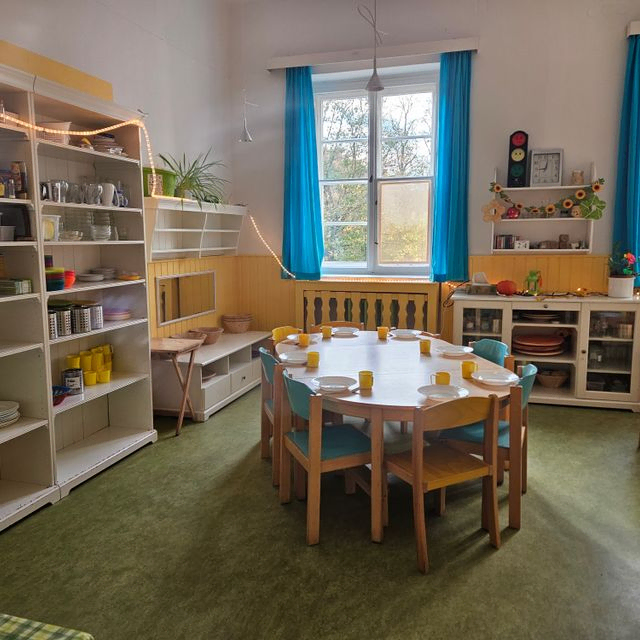 Kinderessbereich mit ovalem Tisch und Regalen in kirchlicher Umgebung.
