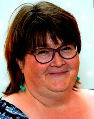 Porträt einer lächelnden Frau mit Brille und türkisen Ohrringen.