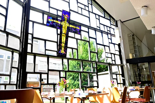 Gemeindesaal mit großem Fenster und Kreuzkunstwerk.