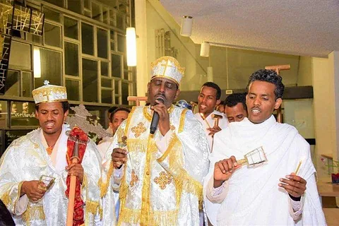 Orthodoxe Priester in Gewändern, einer hält ein Kreuz, ein anderer ein Weihrauchfass.