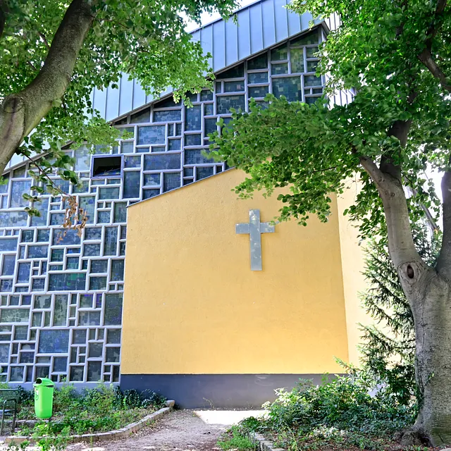Modernes Kirchengebäude außen mit gelber Wand und Kreuz.